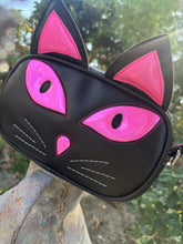 Load image into Gallery viewer, Black cat-shaped bag with pink accents on a stone jug