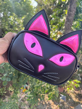 Load image into Gallery viewer, Black cat-shaped purse with pink accents held in front of a green leafy background
