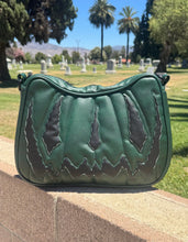 Load image into Gallery viewer, A green quilted shoulder bag with dark brown and light green embroidered mountain-like patterns, resting on a stone wall in an outdoor park setting.