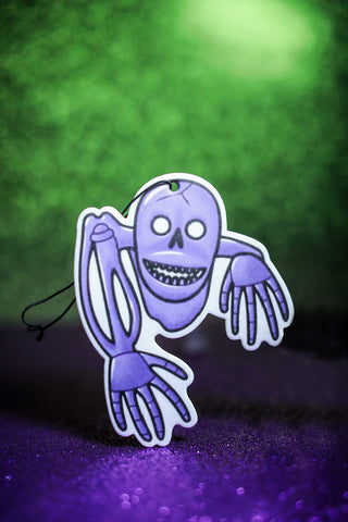 Purple skeleton car air freshener on green background.