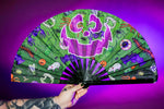 Green fan open with bugs, mice, and jack o lanterns on it, photographed on a purple background. 