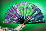 Tattooed hand holding the purple fan with pumpkin face and green background.