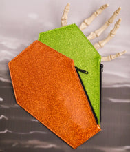 Load image into Gallery viewer, Orange glitter coffin shaped coin bag with a black zipper on top of a green glitter coffin coin bag with a black zipper laying on a skeleton hand