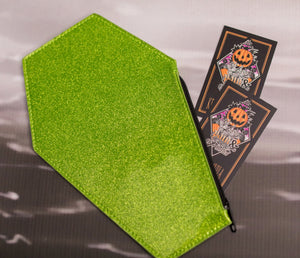 Green glitter coffin shaped coin bag with green stitching and a black zipper with two Love Pain and stitches business cards sticking out 