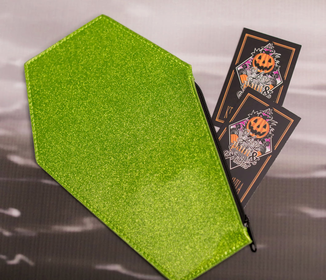 Green glitter coffin shaped coin bag with green stitching and a black zipper with two Love Pain and stitches business cards sticking out 