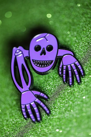 Enamel pin of purple smiling skeleton.