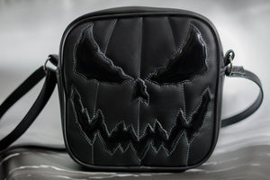 All black square bag with grey stitching on the face , Shiny patent black for the eyes and mouth with a plain black for the body.