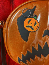 Load image into Gallery viewer, Crying pumpkin keychain in orange and black  on top of the bag in the same design.