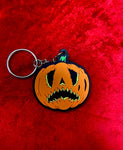 Crying pumpkin keychain in orange and black  on top of a red velvet fabric. 