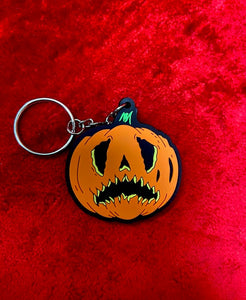Crying pumpkin keychain in orange and black  on top of a red velvet fabric. 
