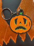 Crying pumpkin keychain in orange and black  on top of the bag in the same design.