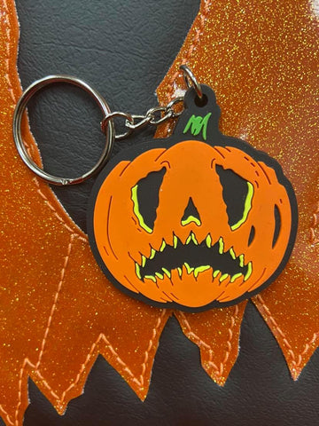 Crying pumpkin keychain in orange and black  on top of the bag in the same design.