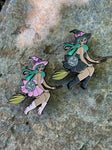 Enamel pins of two witches with mint hair riding brooms.