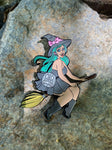 enamel pin of witch in black riding a broom. 