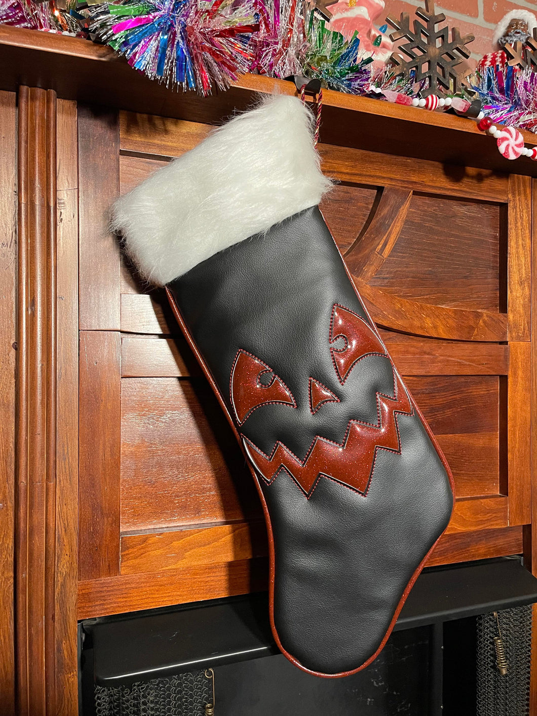 Black holiday stocking with white top, and red glitter edging and jack-o-lantern face.