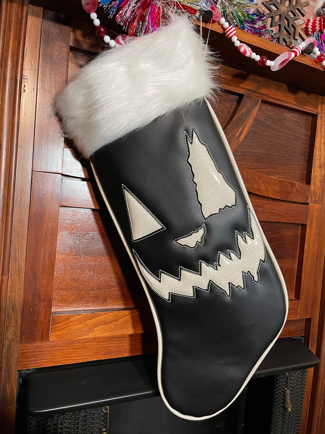 Black holiday stocking with white top, white glitter edging, and white jack-o-lantern face. 