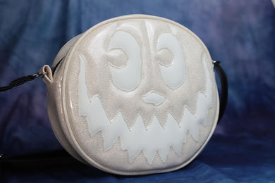 Front view of a round white glitter bag with a matte white smiling jack-o-lantern face that glows-in-in-the-dark.