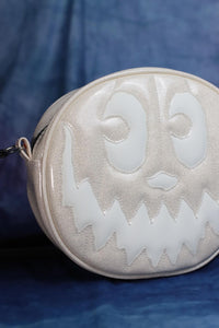 Partial front view of a round white glitter bag with a matte white smiling jack-o-lantern face that glows-in-in-the-dark.