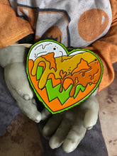 Load image into Gallery viewer, heart shaped pin with candy corn colors and a pumpkin face along with goo drips being held by doll hands