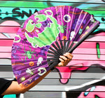 Purple hand fan with images of plastic Halloween toys and a jack-o-lantern face being held open by a hand.