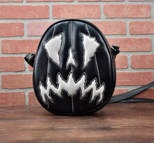 Load image into Gallery viewer, Black and white scaredy-cat face oval pumpkin , white stitching detail on the face handbag. Against a brick wall. 