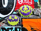 Monster bags photographed against graffiti wall. One in purple and green and the other in green and purple. 