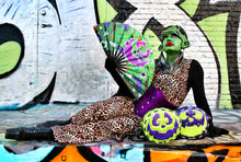 Load image into Gallery viewer, Girl dressed as a monster in front of graffiti wall with two round bags, one in green and purple and the other in purple and green with funny faces