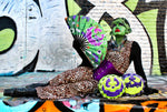 Girl dressed as a monster in front of graffiti wall with two round bags, one in green and purple and the other in purple and green with funny faces